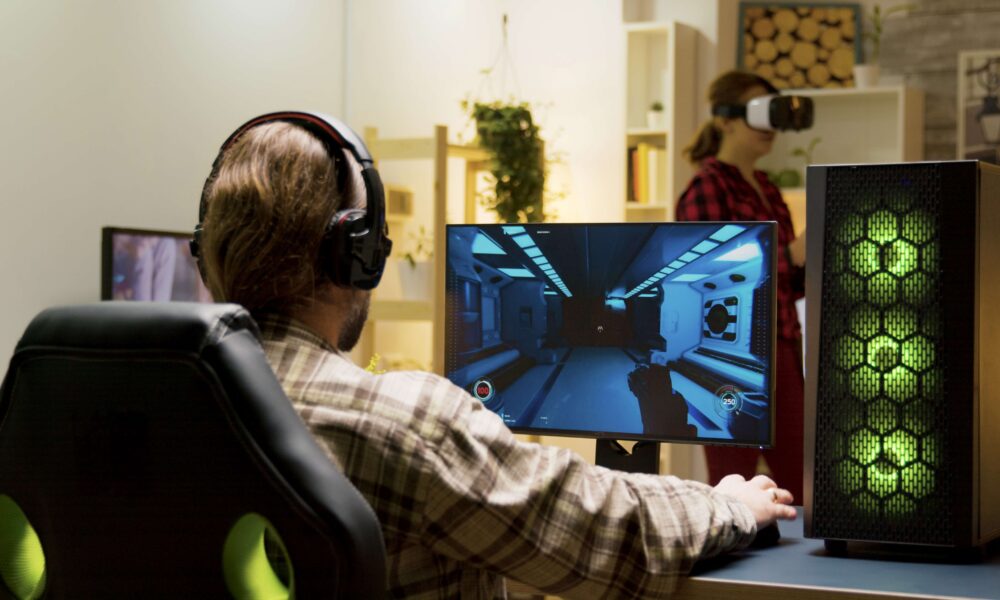 Muškarac sa slušalicama igra indie igre na kompjuteru, a žena u pozadini koristi uređaj za virtuelnu stvarnost.